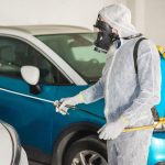 Technician in protective suit applying anti-corrosion spray to a car in a UAE workshop